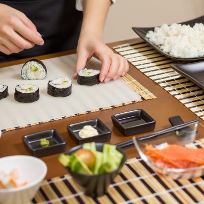 Closeup of woman chef putting japanese sushi rolls with rice, avocado and shrimps on nori seaweed sheet