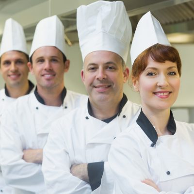 Group of happy chefs smiling at the camera in a kitchen wearing uniforms
